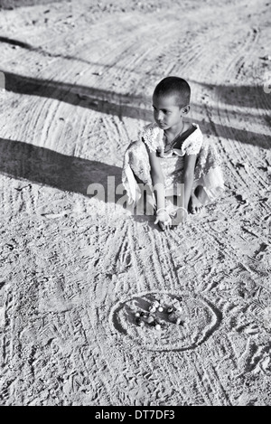 Young Indian girl playing marbles in a rural Indian village. Andhra Pradesh, India.  Selective focus. Monochrome Stock Photo