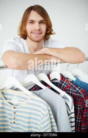 Photo of young man looking at camera by the hangers with clothes Stock Photo
