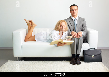 Photo of serious man sitting on sofa with happy woman with open book lying near by Stock Photo