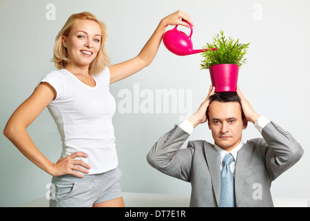 Photo of serious man with plant on head being watered by happy woman Stock Photo