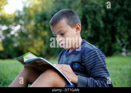 7-year-old boy reading a Christian book in a garden Stock Photo