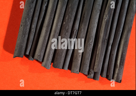 Black charcoal sticks on red paper background. Stock Photo