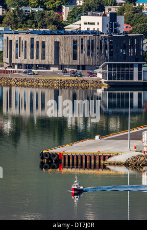 Small Boat in Eyjafordur fjord with HOF Cultural Center and Conference hall in the background,  Akureyi, Iceland Stock Photo