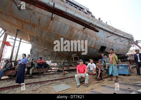 Dock workers sit in front of a vessel under construction during a baptism ceremony of a converted passanger boat, called the 'Swimming Doctors 2' (not in picture), in a dockyard in the capital city of Yangon, Myanmar, 11 February 2014. The vessel, which is owned by the 'Swimming Doctors' foundation, was bapstised by the partner in life of German President Joachim Gauk, Daniela Schadt, and is assigned to supply medical aid and assistance to isolated areas and regions in Myanmar. German German President Gauck is on a four-day visit to Myanmar. Photo: Wolfgang Kumm/dpa Stock Photo