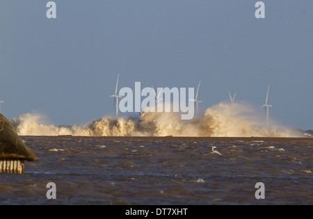 Waves crashing against remains of shingle sea defences with flooded marshes and partially submerged birdwatching hide after Stock Photo