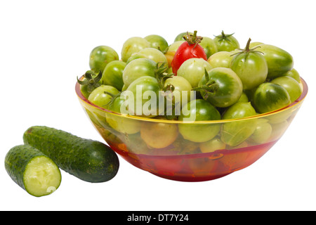 A bowl of green and red tomatoes with some cucumbers near bowl, isolated on white background Stock Photo