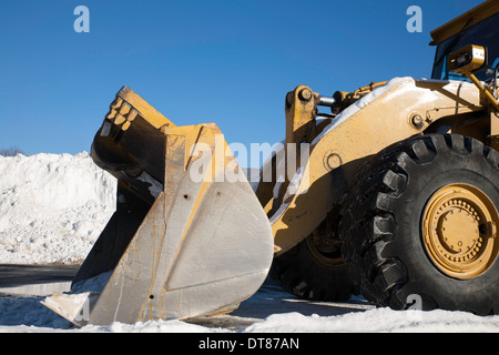 A huge earthmoving machine waits in a New England shopping mall parking lot piled high with recent snow. Stock Photo
