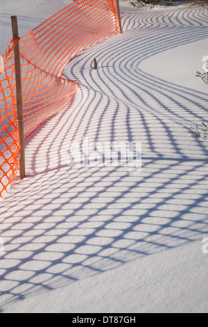 Shadows from an orange plastic snow fence make patterns on the New England snow.