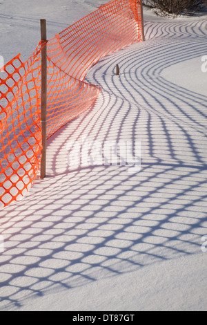 Shadows from an orange plastic snow fence make patterns on the New England snow.