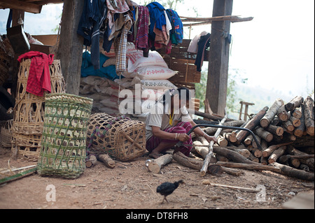 Karen villager sawing wood in the base of a typical Karen villager's wooden stilted house. Stock Photo