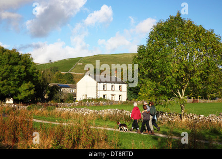 A family walking their dog on the footpath beside a dry stone wall and cottage. Stock Photo