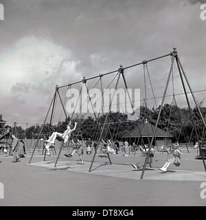 Historical picture from 1960s showing school children enjoying the traditional type swings in a recreational playground. Stock Photo