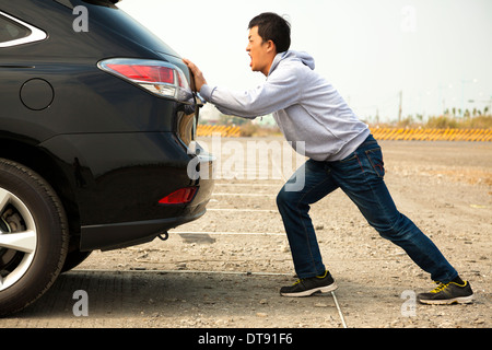 Asian Man pushing a broken car down the rock road Stock Photo