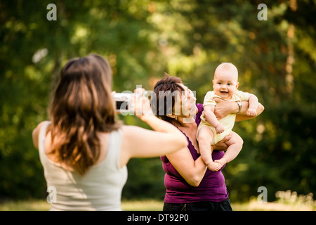 Mother taking photo of grandmother holding her granddaughter - outdoor in nature Stock Photo