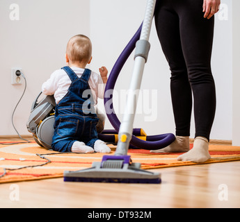 Cleaning up the room - woman with vacuum cleaner, baby sitting on floor Stock Photo