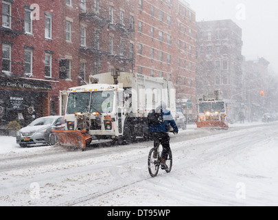 A man riding a bicycle in the East Village of New York with snow plows running down the street. (Avenue A) Stock Photo