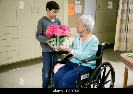 Grandson gives his Elderly Hispanic grandmother  in a wheelchair, a bouquet of flowers while she is at a rehabilitation hospital Stock Photo