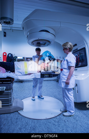 Nurses putting a mesh mask on cancer patient just prior to radiation treatment. Male patient is under a linear accelerator. Stock Photo