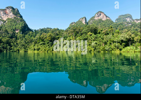 Forested karst limestone mountains with jungle vegetation reflected in the water, Rachabrapha reservoir, Chiao Lan Lake Stock Photo