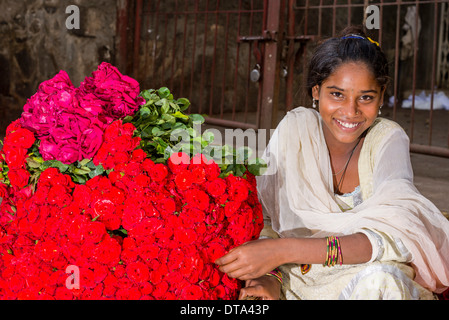 A smiling young woman in a white sari is selling red roses at the weekly market, Nasik, Maharashtra, India Stock Photo