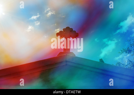 Mausoleum cross against blue sky. Bright sunlight lens flare through painted glass digital composite abstract blur. Stock Photo