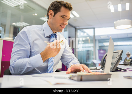 Businessman eating sushi in office Stock Photo