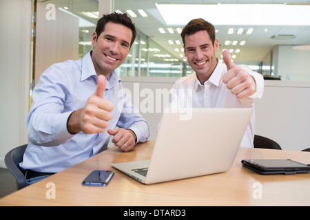 Successful smiling businessmen in office, looking camera, giving thumbs up Stock Photo