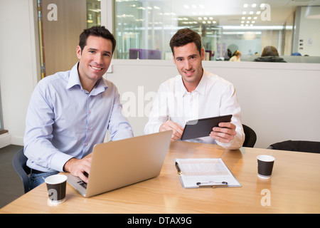 Two casual businessmen working in office with laptop and tablet, looking camera Stock Photo