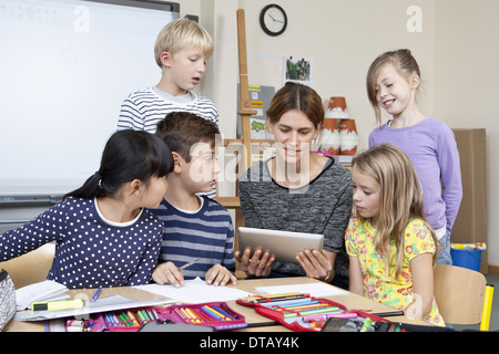 Teacher using digital tablet with students in classroom Stock Photo