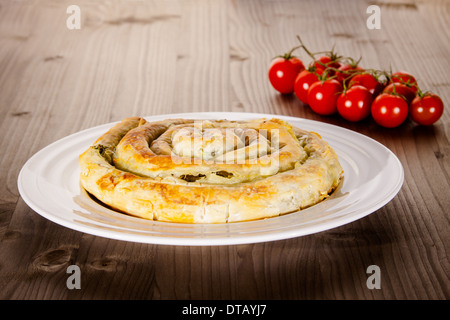 Spinach and cheese pie on white plate with tomatoes in background Stock Photo