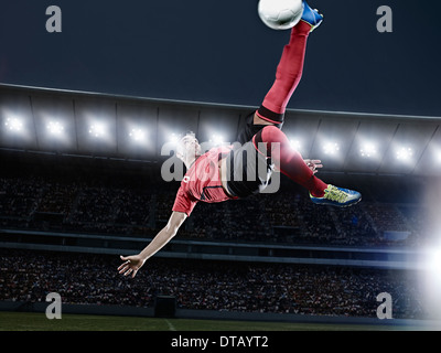 Soccer player kicking ball in mid-air on field Stock Photo
