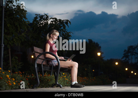Young woman sitting on park bench and using laptop Stock Photo