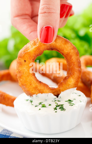 Small Inion Hand holding a fried onion ring above a small container of dipping ...