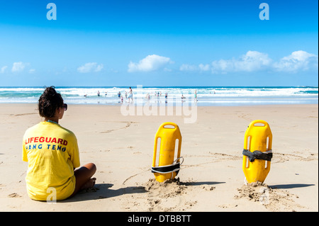 A lifeguard with rescue equipment sitting on the beach watching swimmers in the sea, Sedgefield, Eastern Cape, South Africa Stock Photo