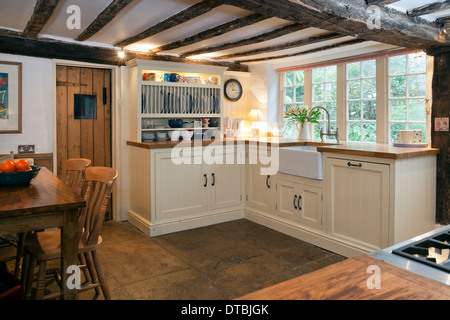 Period beamed ceiling small kitchen with paint finished fitted units and butler sink. Stock Photo