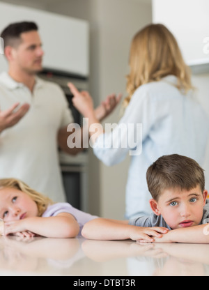 Sad children leaning on table while parents arguing Stock Photo