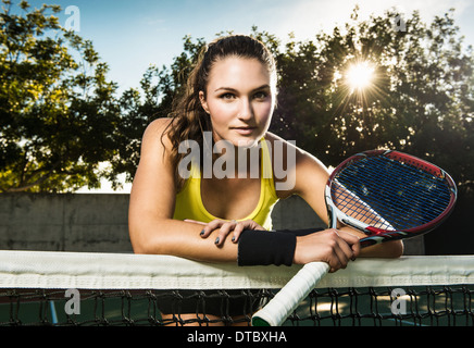 Female tennis player holding racket leaning on net Stock Photo