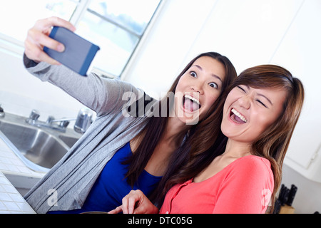 Two young women in kitchen taking self portrait with mobile phone Stock Photo