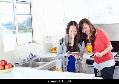 Two young women in kitchen looking at digital tablet Stock Photo