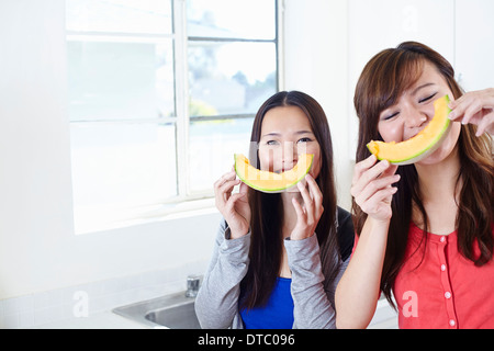 Two young women in kitchen with melon smiley faces Stock Photo