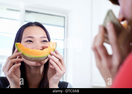 Two young women in kitchen with melon mouths Stock Photo