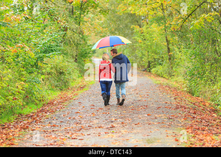 Young couple strolling along country lane with colorful umbrella Stock Photo