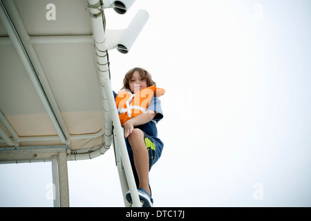 Young boy in life jacket climbing up boat steps Stock Photo