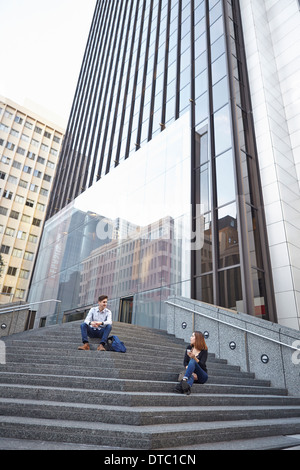 Mid adult man chatting up young woman whilst sitting on steps Stock Photo