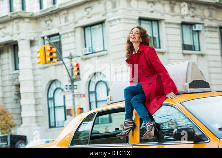 Young female tourist sitting on top of yellow cab, New York City, USA Stock Photo