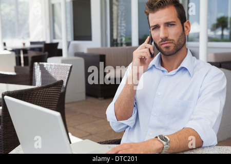 Frowning businessman talking on phone using his laptop Stock Photo