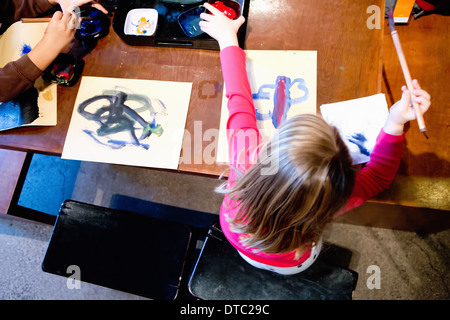 Two young siblings painting pictures at table