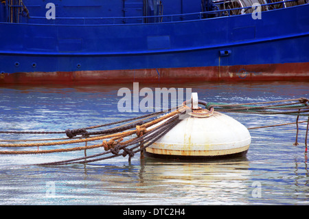 rusty buoy with lot of ropes and a ship on port Stock Photo