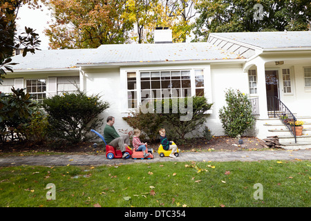 Father and young sons riding on toy cars in garden Stock Photo