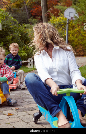 Mother and young sons riding on toy cars in garden Stock Photo